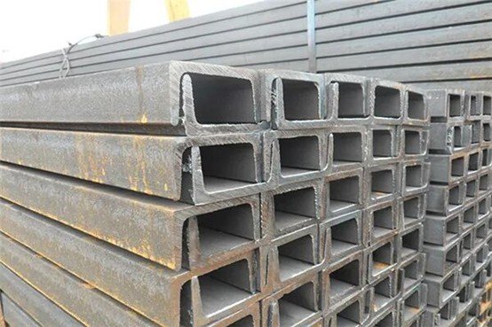 A stack of steel channel sections neatly arranged on the workshop floor, waiting to be cut by the bandsaw blade.